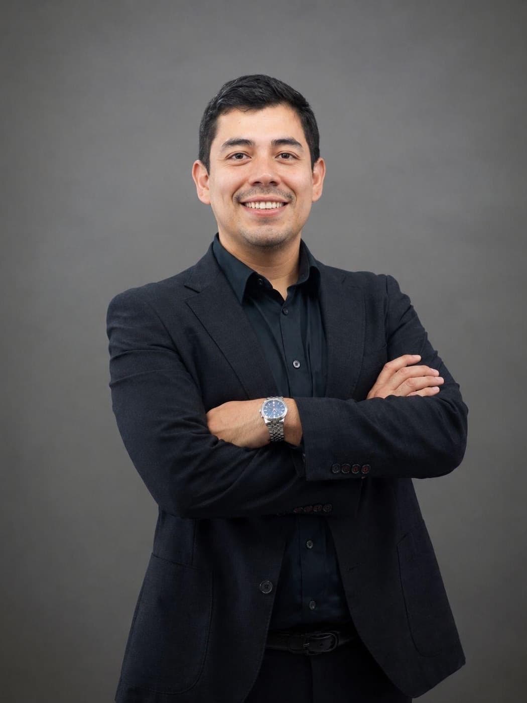Samuel García, socio de SinergIA 180°, de pie con los brazos cruzados, saco y camisa oscuros, sonriendo a la cámara.