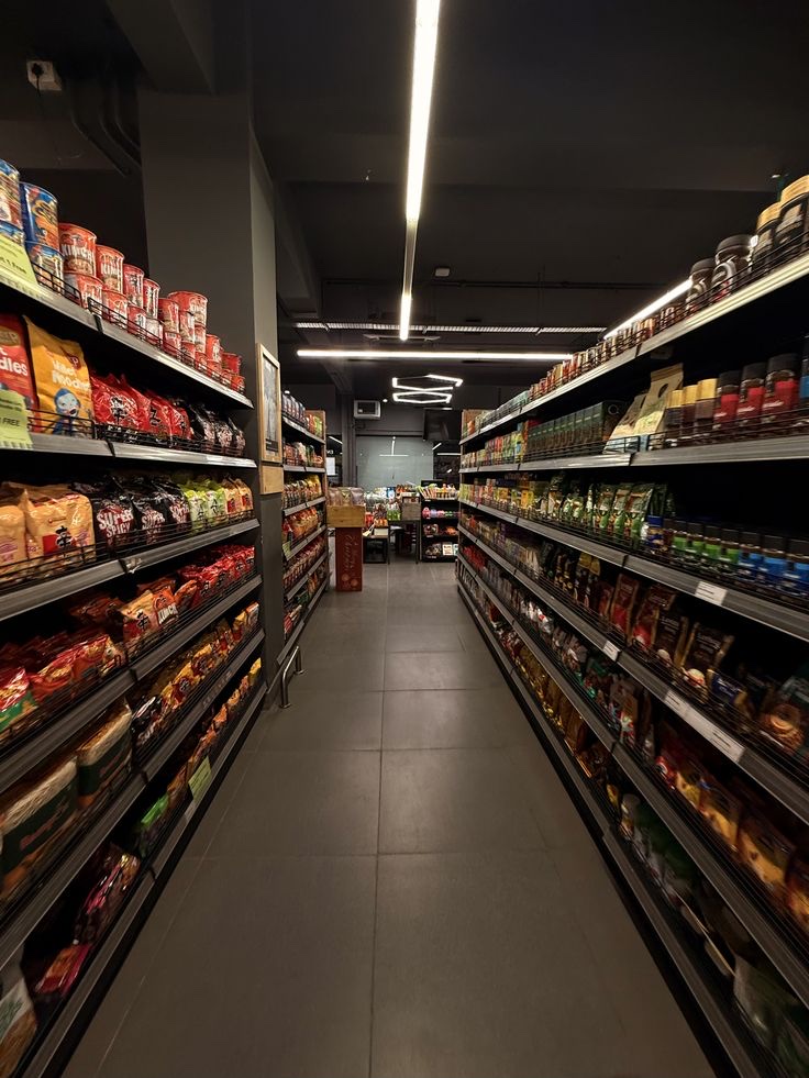 Pasillo de un supermercado con las góndolas llenas de productos envasados a ambos lados y luz lineal en el techo.